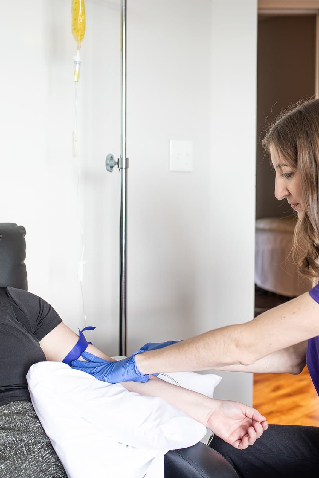 Practitioner in blue gloves administering IV therapy to a patient's arm in a clinical treatment room