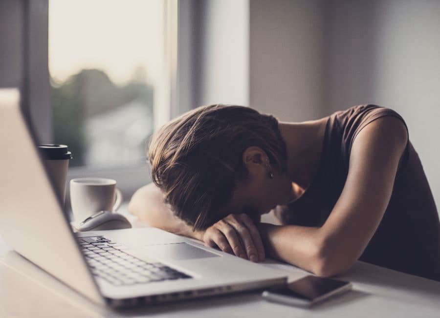 Person with head down on desk next to laptop, experiencing fatigue or burnout
